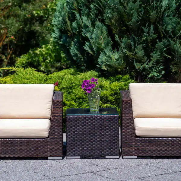 Outdoor patio with two white cushioned chairs and a small table with purple flowers.