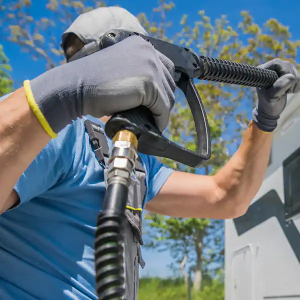 Power washing a vehicle with a high-pressure hose outdoors on a sunny day.